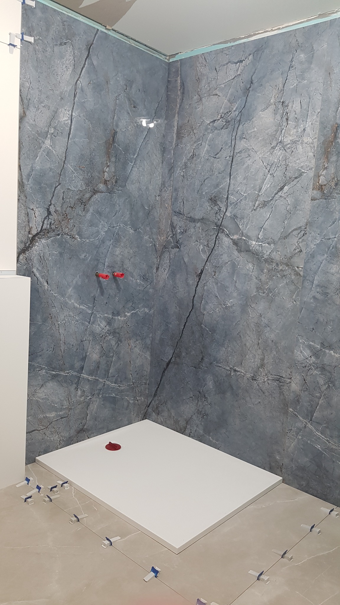 Montaż brodzika z odpływem w kolorze czerwonym i płytek imitujących marmur w odcieniach szarości, z użyciem klipsów poziomujących.