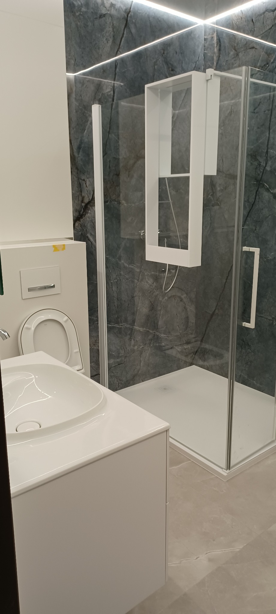 Nowoczesna łazienka z kabiną prysznicową typu walk-in, umywalką nablatową i toaletą w zabudowie, wykończona płytkami imitującymi marmur w odcieniach szarości.