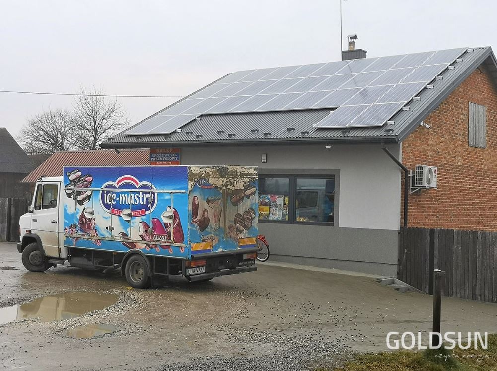 Budynek sklepu z panelami słonecznymi na dachu, obok zaparkowany samochód dostawczy z reklamą lodów.