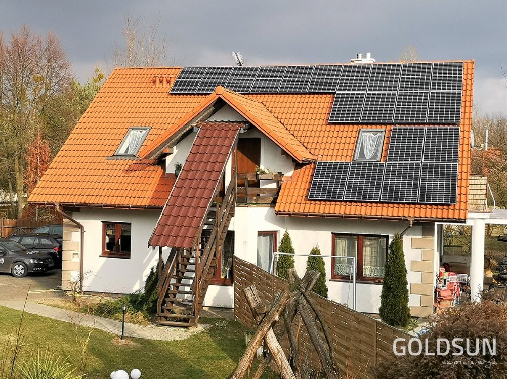 Dom jednorodzinny z pomarańczową dachówką i panelami słonecznymi na dachu, dodatkowe schody zewnętrzne prowadzące na balkon.