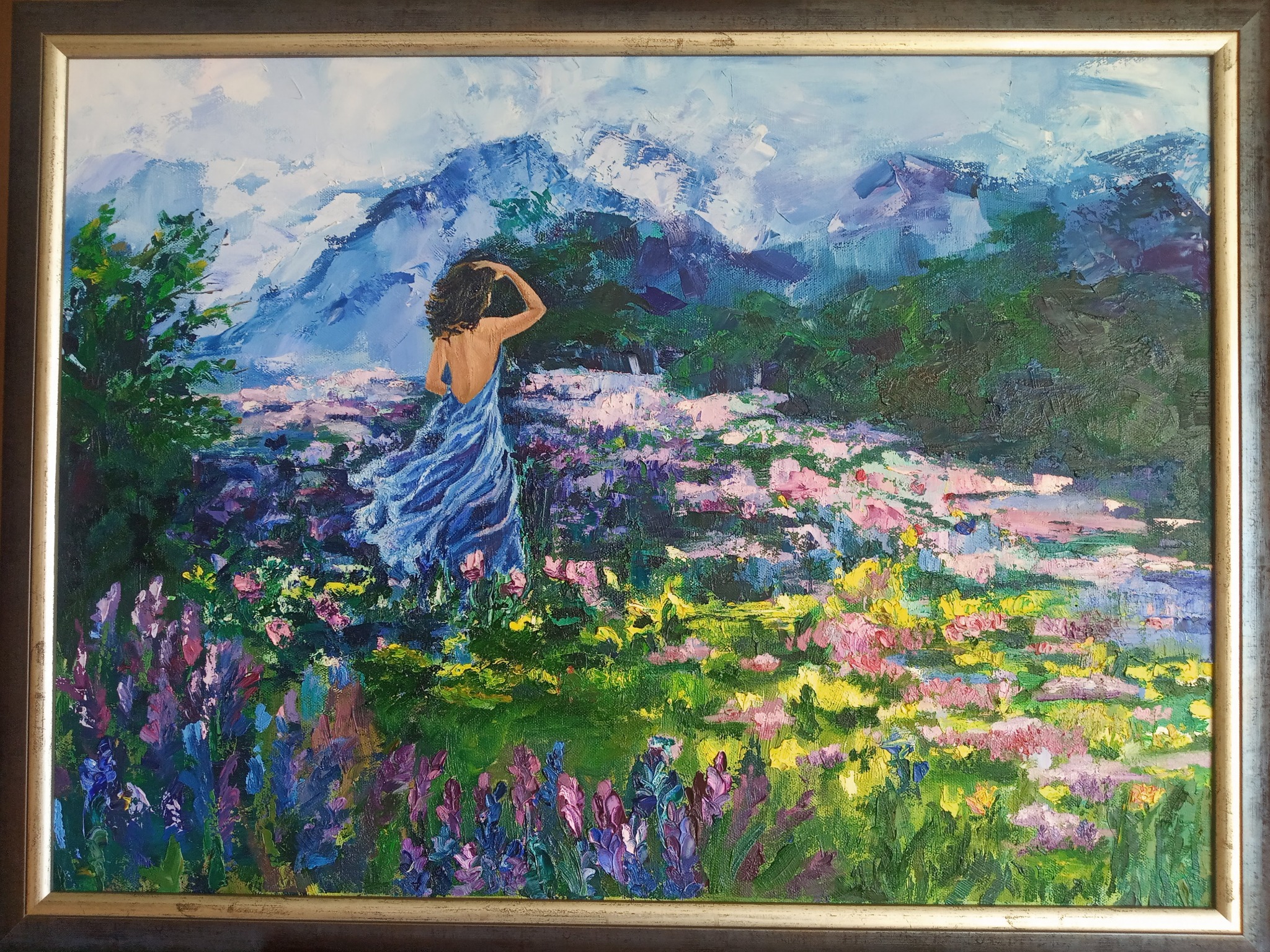 Impresjonistyczny obraz olejny przedstawiający kobietę w błękitnej sukience stojącą tyłem na łące pełnej kwiatów z górami w tle, namalowany grubymi pociągnięciami pędzla w jasnych kolorach...