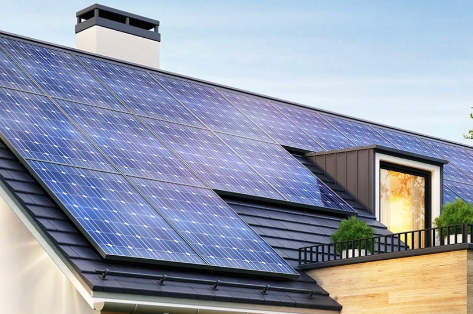 Panel słoneczny na dachu domu z oknem mansardowym, widok z dołu, błękitne niebo w tle.