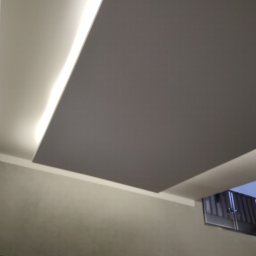 Firma Budowlana MatBud - Sufit podwieszany z oświetleniem LED wzdłuż krawędzi, szara płaszczyzna sufitu, widok na fragment okna w tle.