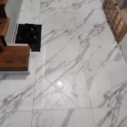 Nowoczesna podłoga z płytek imitujących marmur z widocznymi schodami z ciemnego drewna, czarną wycieraczką z butami i świeczką w szklanym pojemniku.