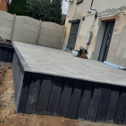 Firma Budowlana MatBud - Wykonana izolacja pionowa fundamentów z płyt styropianowych, zabezpieczona szarą kostką brukową, widoczne fundamenty budynku w trakcie prac ziemnych.