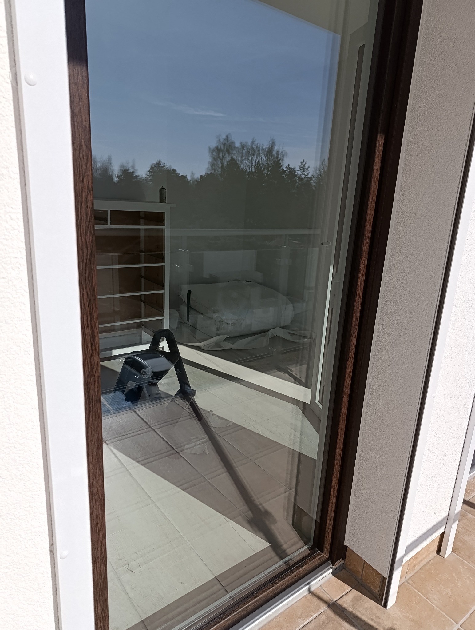 Okno balkonowe po umyciu, widoczny sprzęt do mycia szyb. Czyste okno odbija drzewa i niebo. Usługi porządkowe w Aleksandrowie Łódzkim.