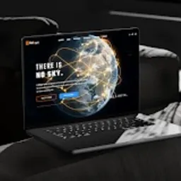 Laptop na ciemnej sofie prezentujący stronę internetową z motywem globalnej sieci połączeń i hasłem 'THERE IS NO SKY.'
