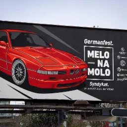 Billboard reklamujący wydarzenie Germanfest z ilustracją czerwonego BMW E31, hasłem 'MELO NA MOLO' i logotypami sponsorów, umieszczony w miejskiej przestrzeni.
