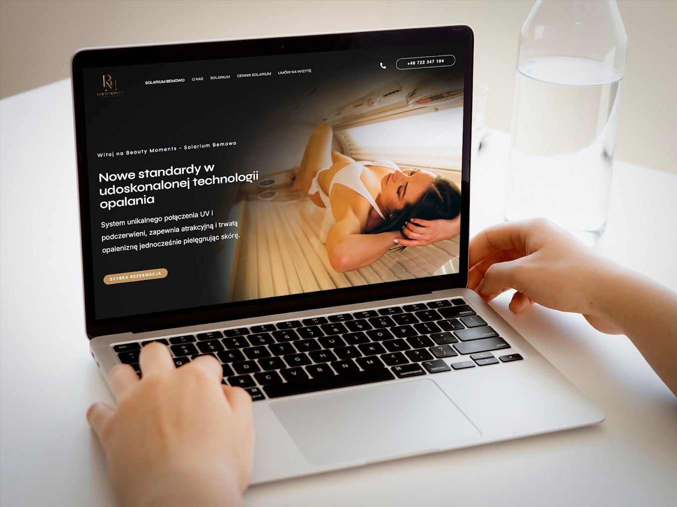 Osoba przegląda na laptopie stronę internetową solarium Beauty Moments z ofertą opalania w solarium, widoczna kobieta opalająca się w solarium.