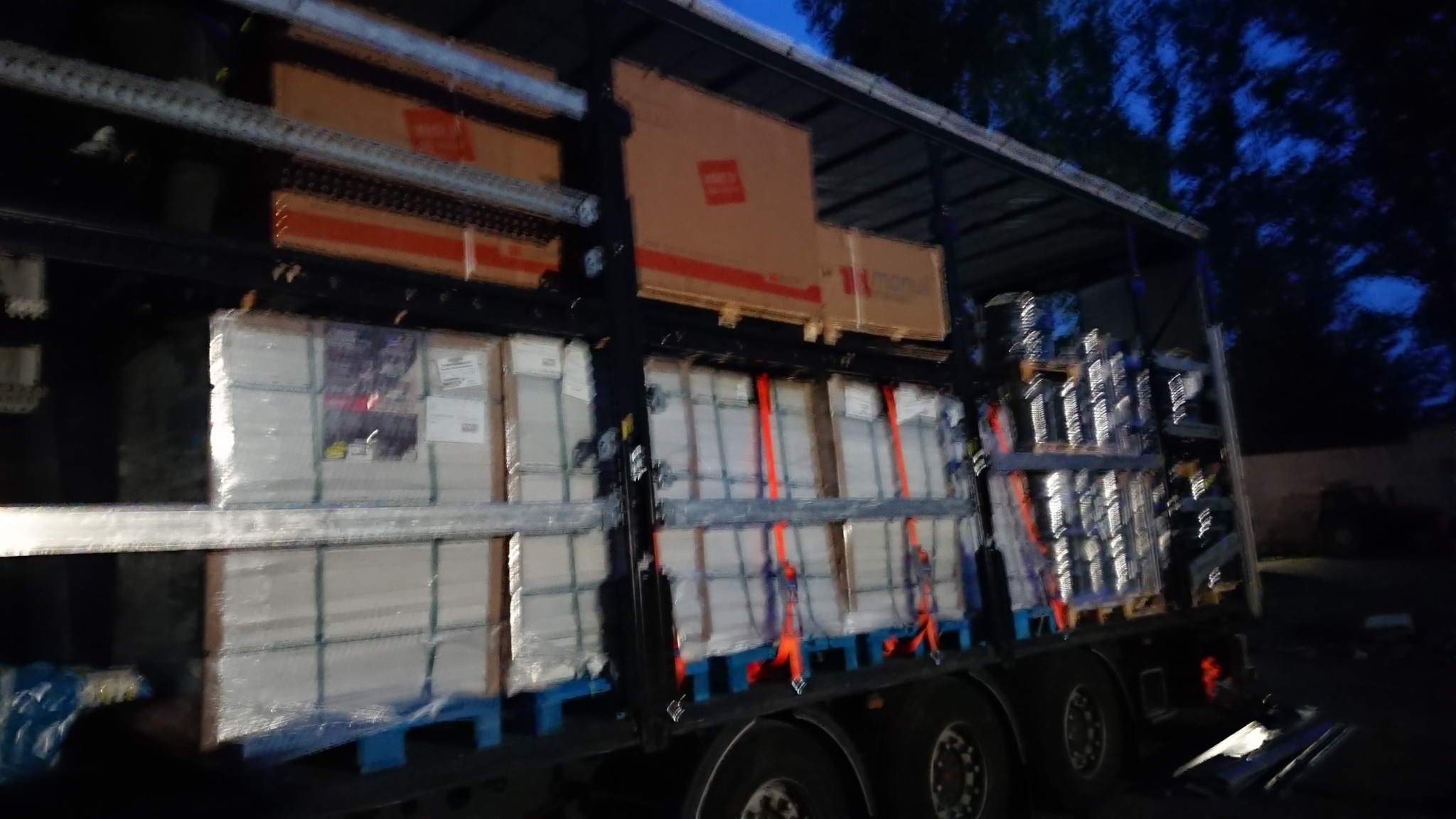 Ciężarówka załadowana paletami z towarem, zabezpieczonymi pasami transportowymi, w trakcie nocnego transportu.