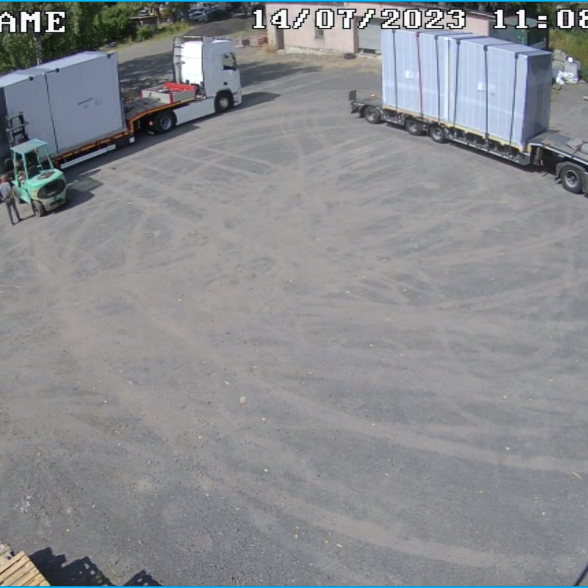 Transport dwóch ciężarówek z ładunkami zabezpieczonymi folią, jedna rozładowywana wózkiem widłowym, widok z góry.