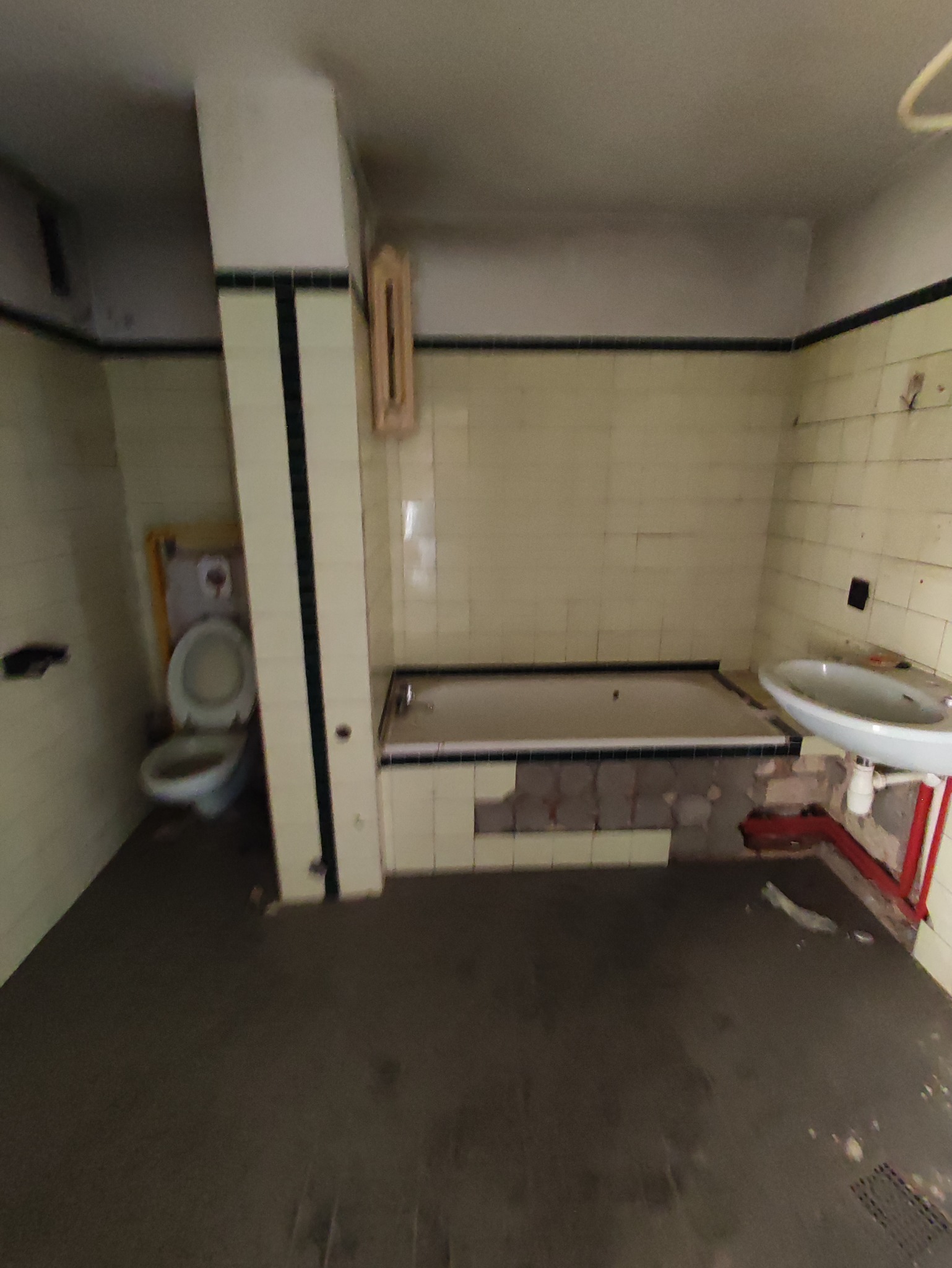 Łazienka w trakcie demontażu w Sędzimirowie: usunięte fragmenty płytek przy wannie, widoczne rury, toaleta, umywalka i pozostałości starej glazury.