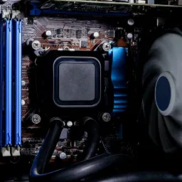 Wnętrze komputera stacjonarnego z chłodzeniem wodnym, widoczne niebieskie kości RAM i płyta główna. Detaliczne ujęcie na podzespoły PC.