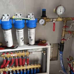 Instal-Mix - Rozbudowana instalacja hydrauliczna z filtrami wody, manometrami i rozdzielaczem ogrzewania podłogowego w szafce, widoczne narzędzia monterskie.