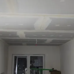 Sufit z płyt kartonowo-gipsowych, przygotowany do malowania, ze szpachlowanymi łączeniami i listwami dekoracyjnymi przy ścianach.