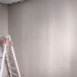 Prof Bud - Przygotowanie do malowania: Ściana po usunięciu starej farby, widoczne ślady po skrobaniu, drabina oparta o ścianę, gruz na podłodze, narożnik sufitu z widocznymi uszkodzeniami.