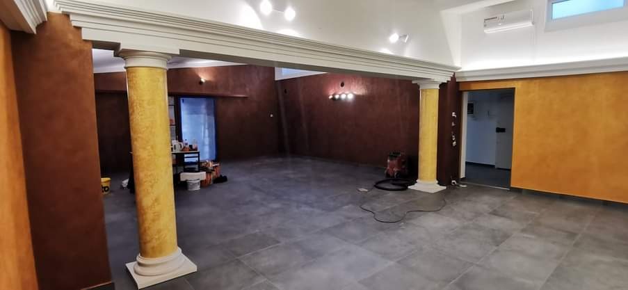 Przestronne wnętrze po remoncie: szare płytki podłogowe, kolumny w kolorze złota, ściany w odcieniach brązu i pomarańczy, widoczne ślady po pracach wykończeniowych.