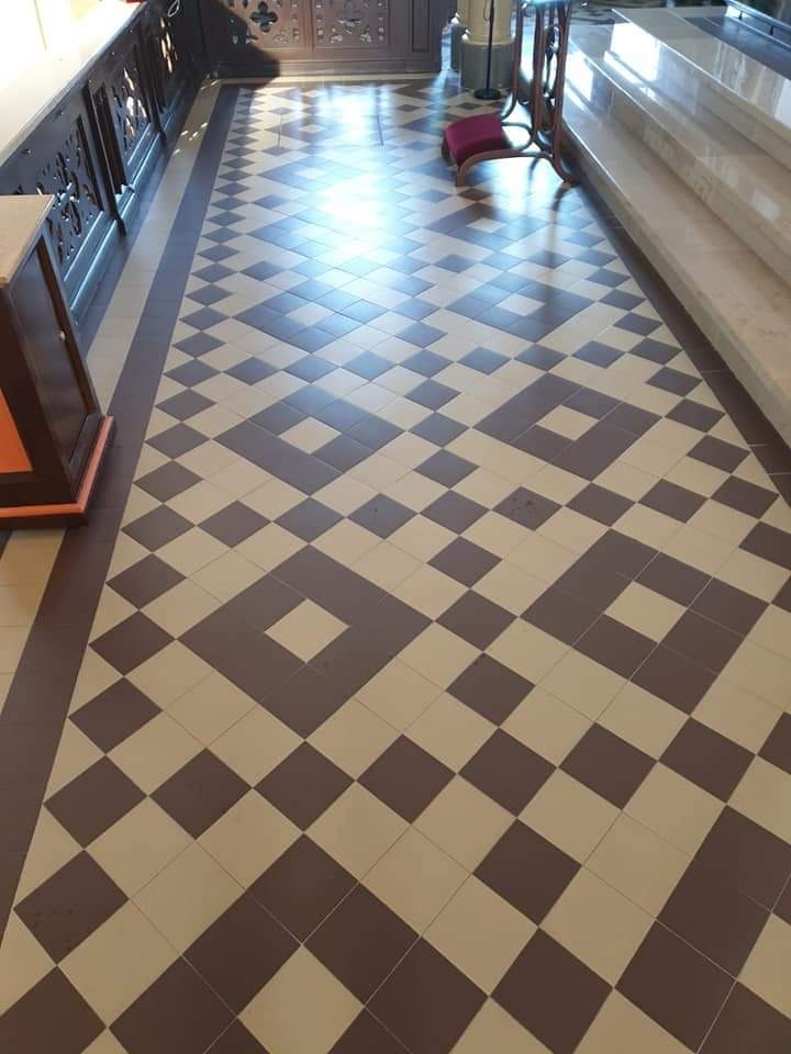 Wzorzysta posadzka z kwadratowych płytek w odcieniach brązu i beżu, ułożonych w geometryczny deseń, widoczny fragment balustrady i schodów.