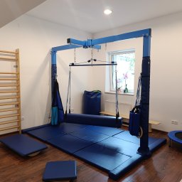 Logo.Pasja - Gabinet terapeutyczny JOANNA SIEREŃSKA - Sala do integracji sensorycznej z drabinką, podwieszanym sprzętem do ćwiczeń, matami i trampoliną. Jasne wnętrze, sprzęt w odcieniach niebieskiego.