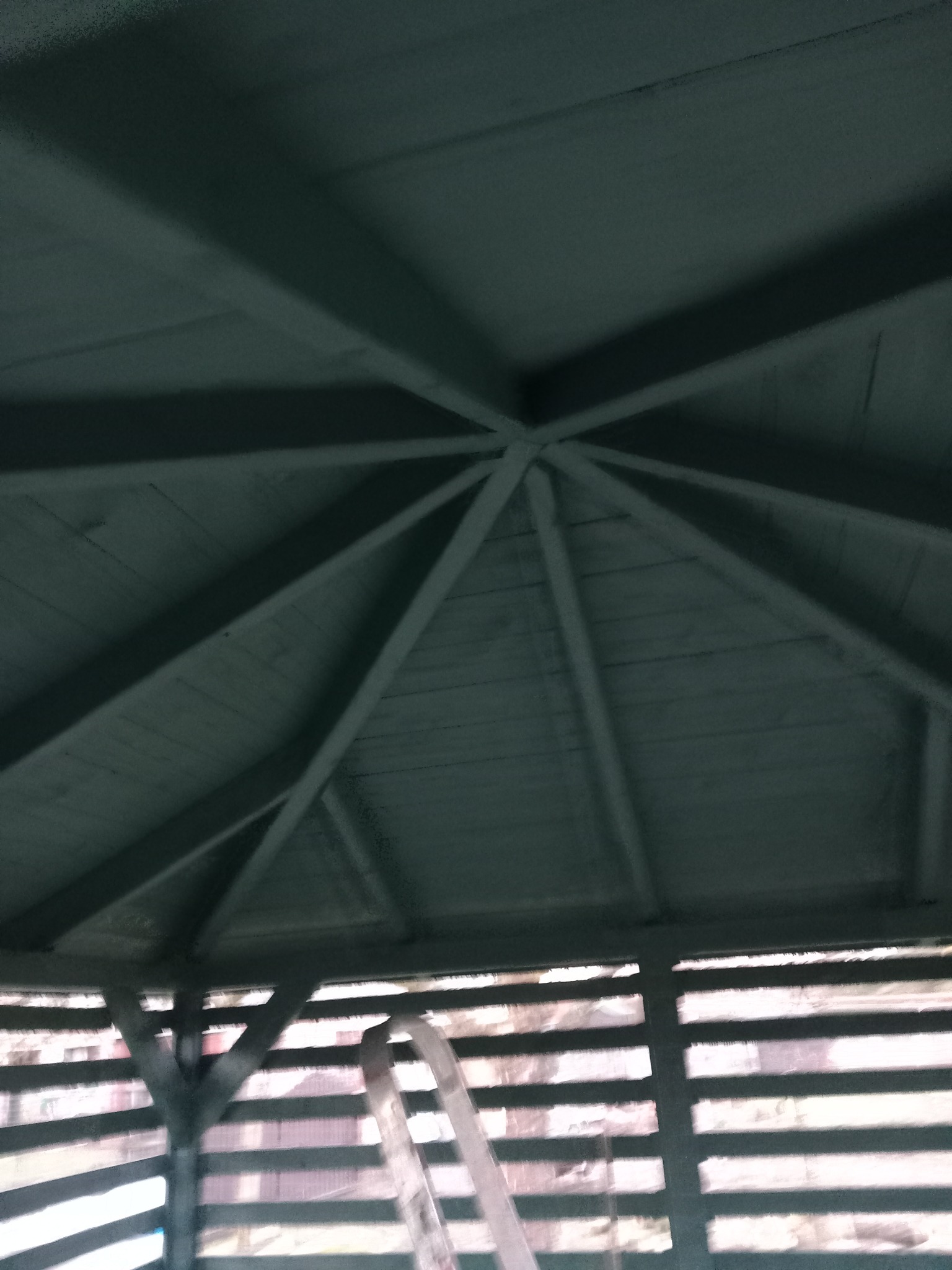 Wnętrze pomalowanej na szaro altany z widoczną konstrukcją dachu i fragmentem drabiny opierającej się o jej bok.