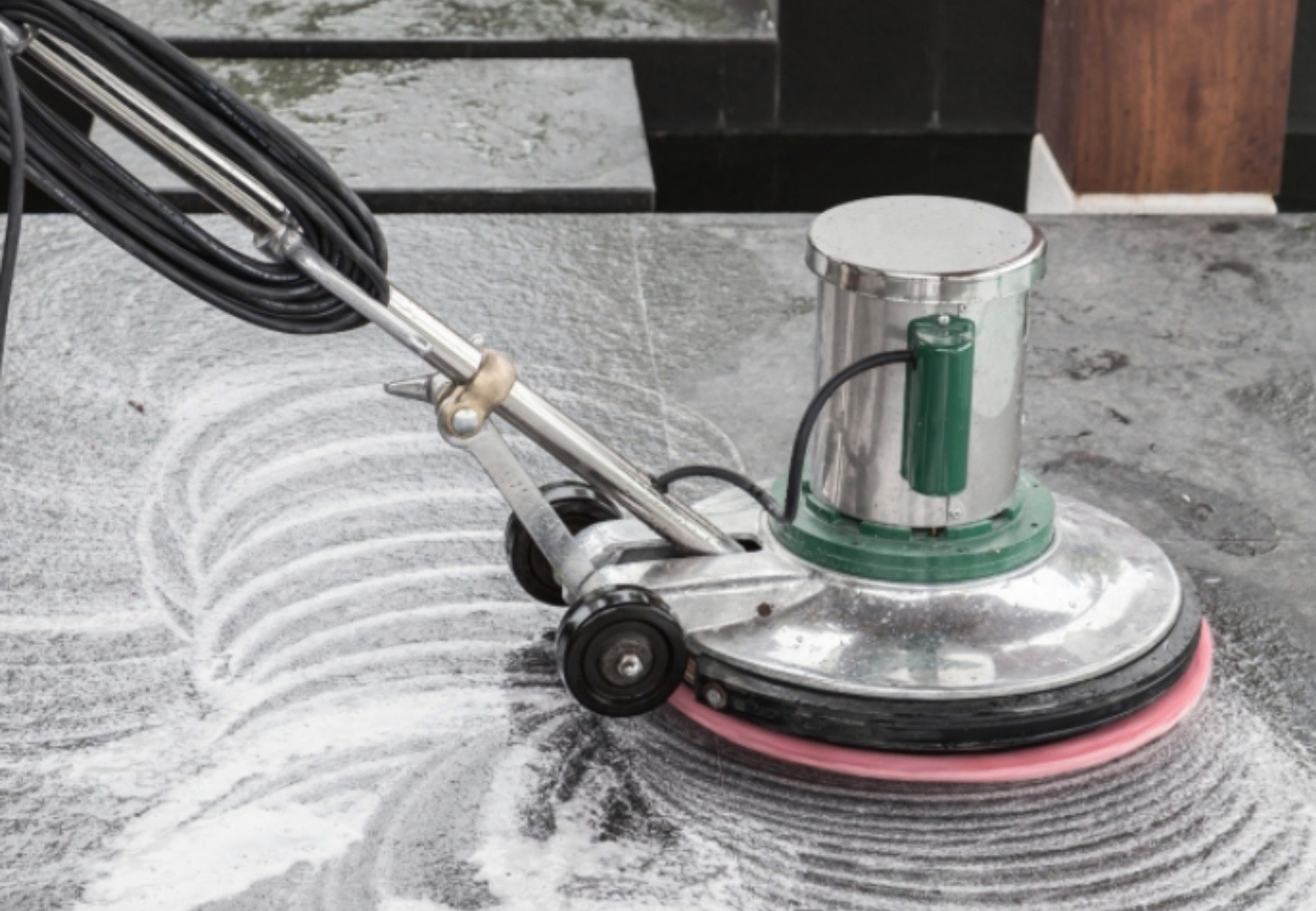 Profesjonalna maszyna do czyszczenia kostki brukowej w trakcie pracy, pozostawiająca za sobą ślady piany na szarej powierzchni.