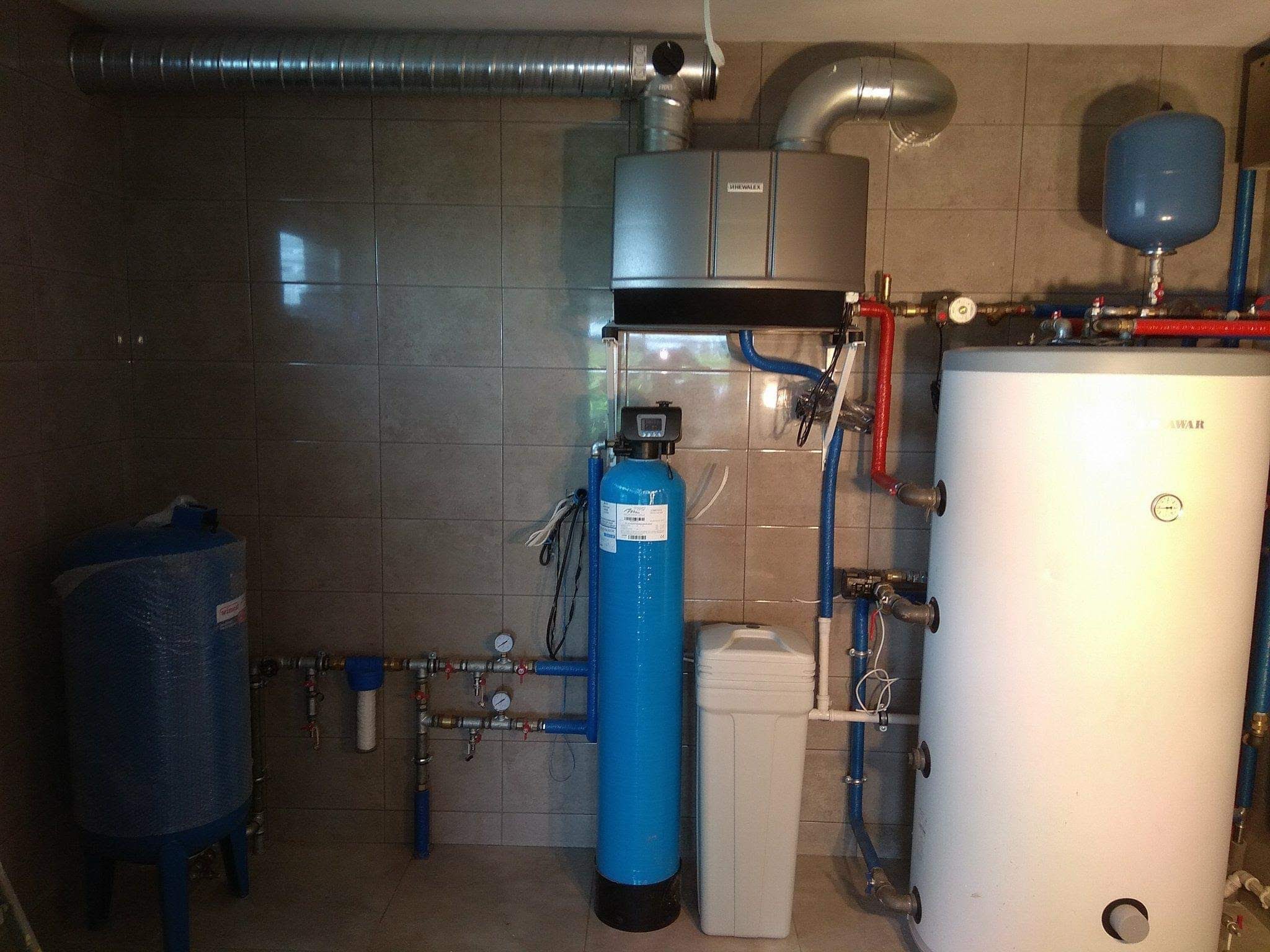 Kotłownia z piecem gazowym, zasobnikiem ciepłej wody, filtrem narurowym i zmiękczaczem wody, instalacja w szarych płytkach.
