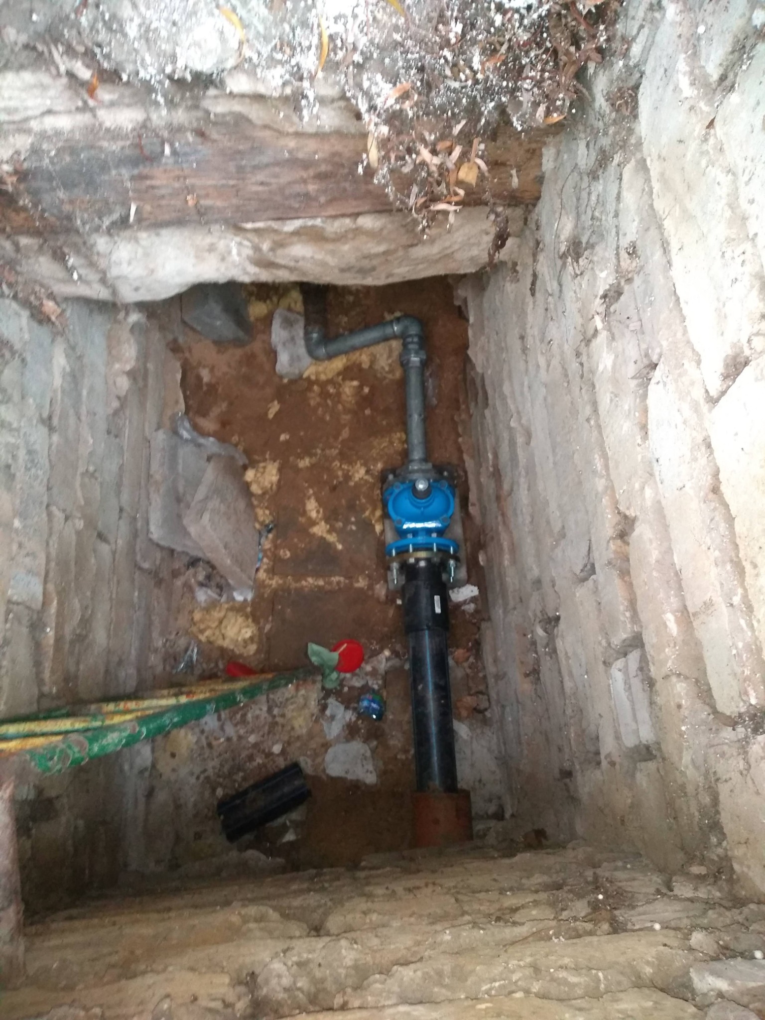 Wykonane przyłącze wodociągowe z niebieskim zaworem i czarną rurą w wykopie o ścianach z kamienia i ziemi.