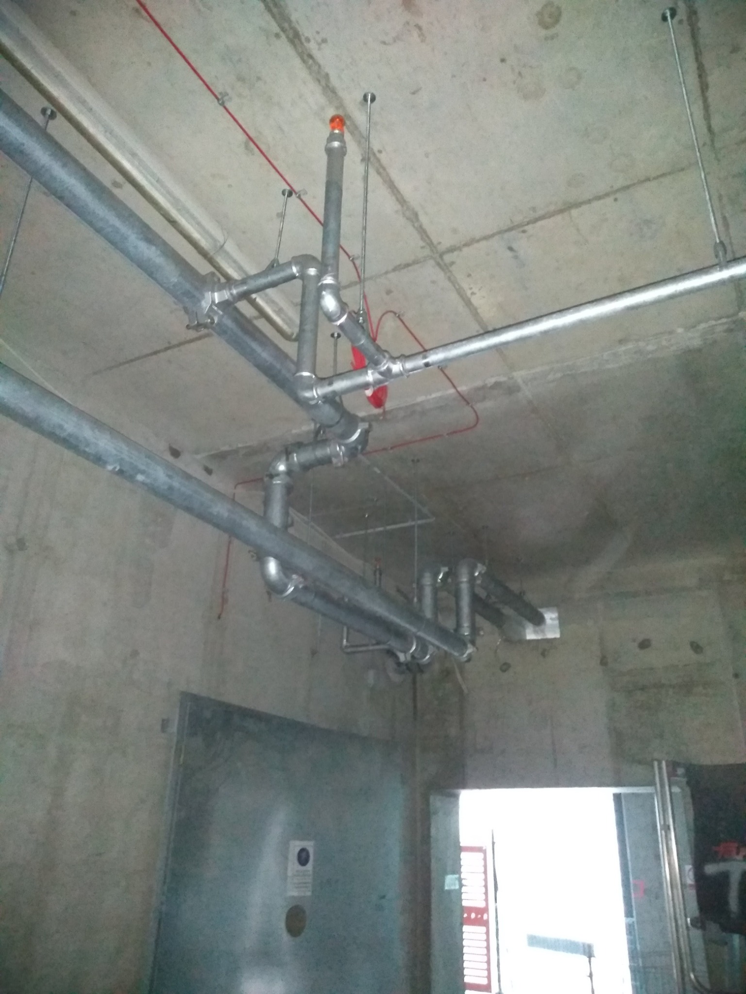 Szare, metalowe rury instalacyjne pod betonowym sufitem z widocznymi mocowaniami i elementami sygnalizacyjnymi w nowym budynku, widok z dołu.