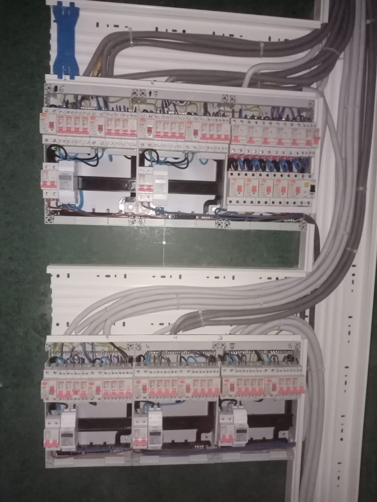 Rozdzielnica elektryczna z licznymi zabezpieczeniami i przewodami, widoczne bezpieczniki i kable w peszlach, całość zamontowana wewnątrz białej obudowy.