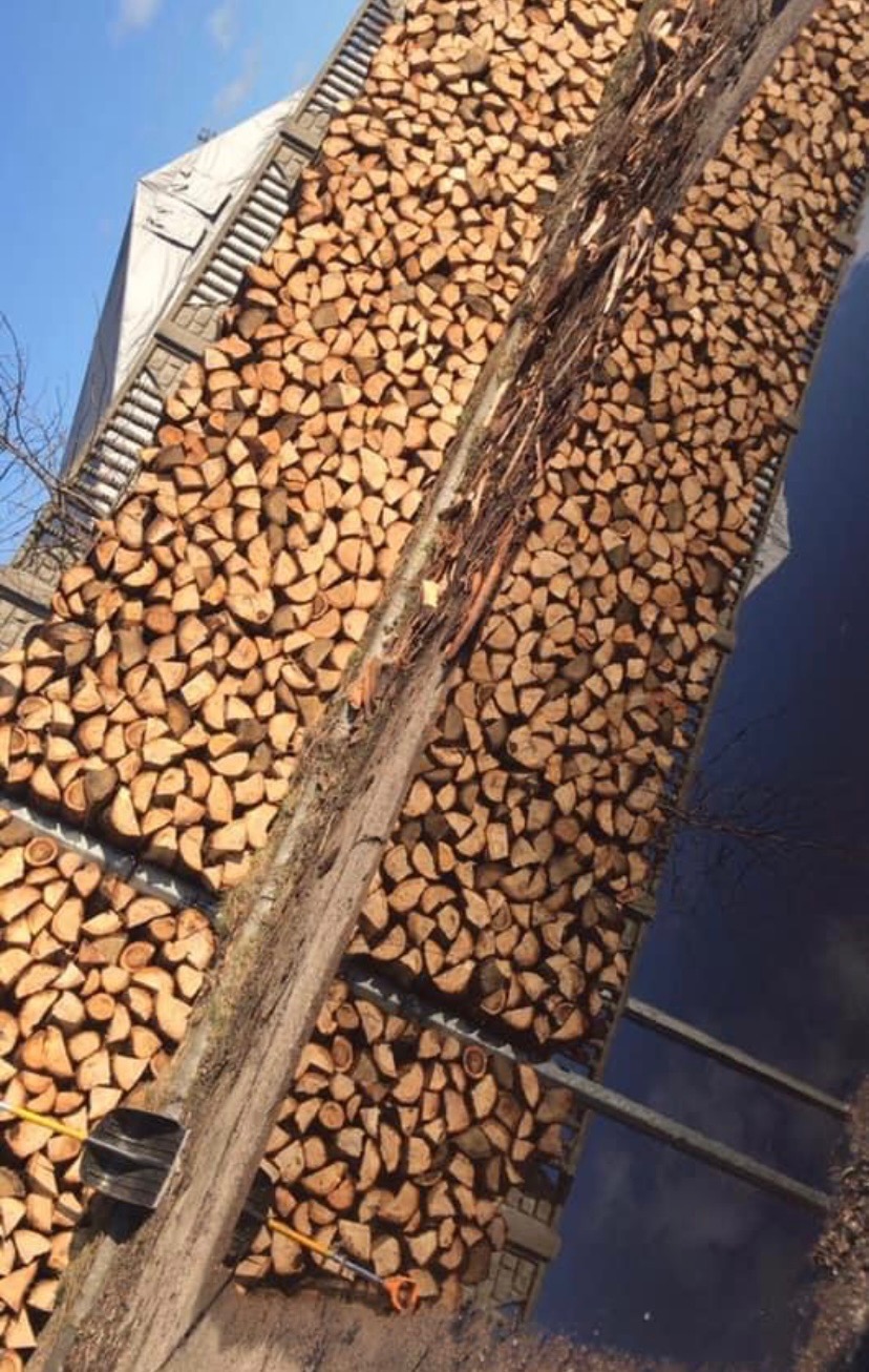 Rząd ułożonego drewna na opał, widoczne narzędzia, w tle błękitne niebo