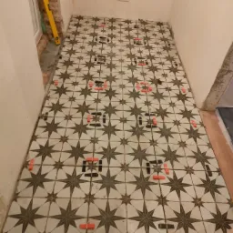 Układanie podłogi z płytek w gwiazdy, widoczne poziomica i krzyżyki dystansowe, surowy stan ścian.