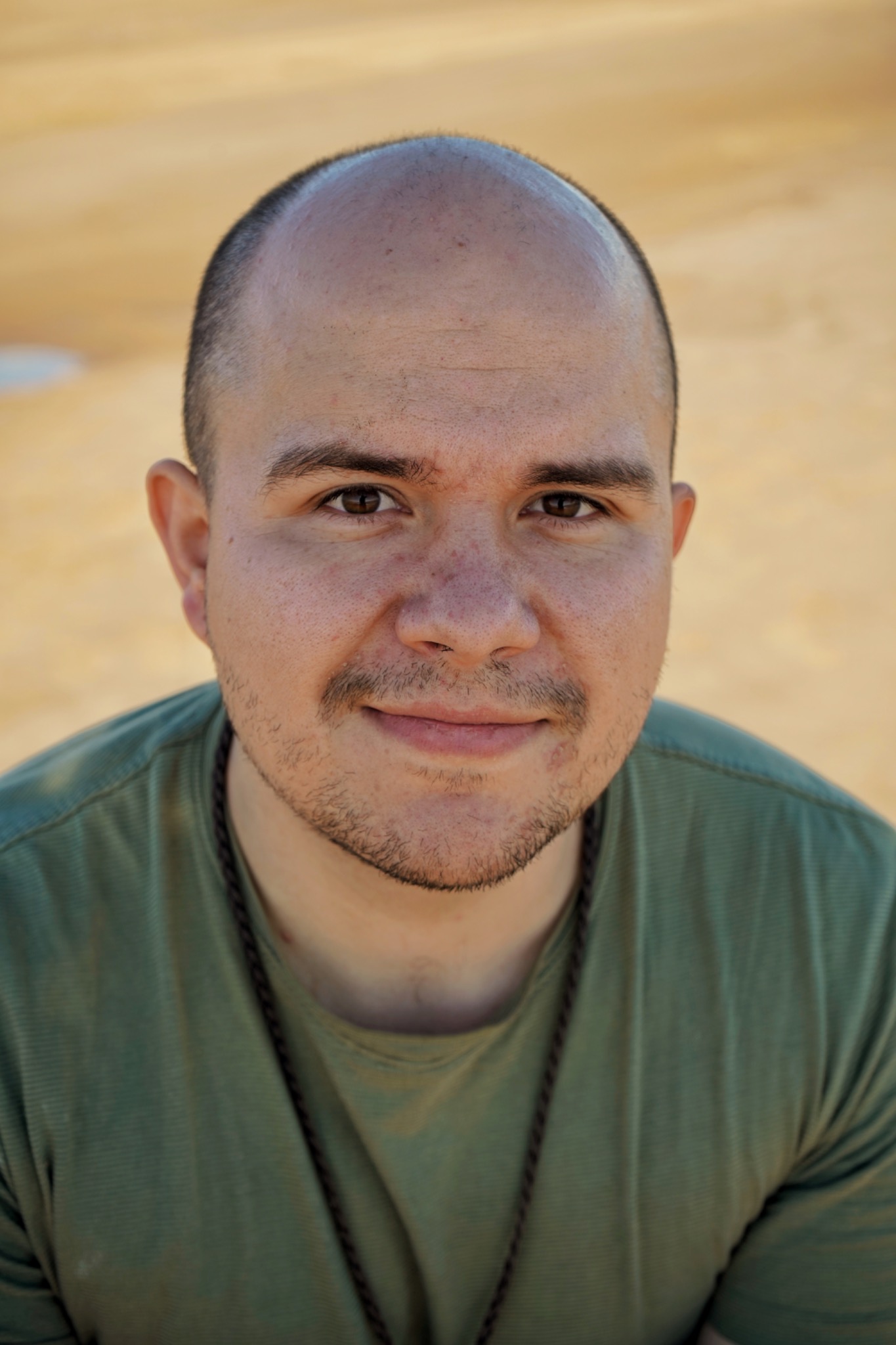 Portret mężczyzny w zielonej koszulce z delikatnym uśmiechem, na rozmytym, jasnym tle.