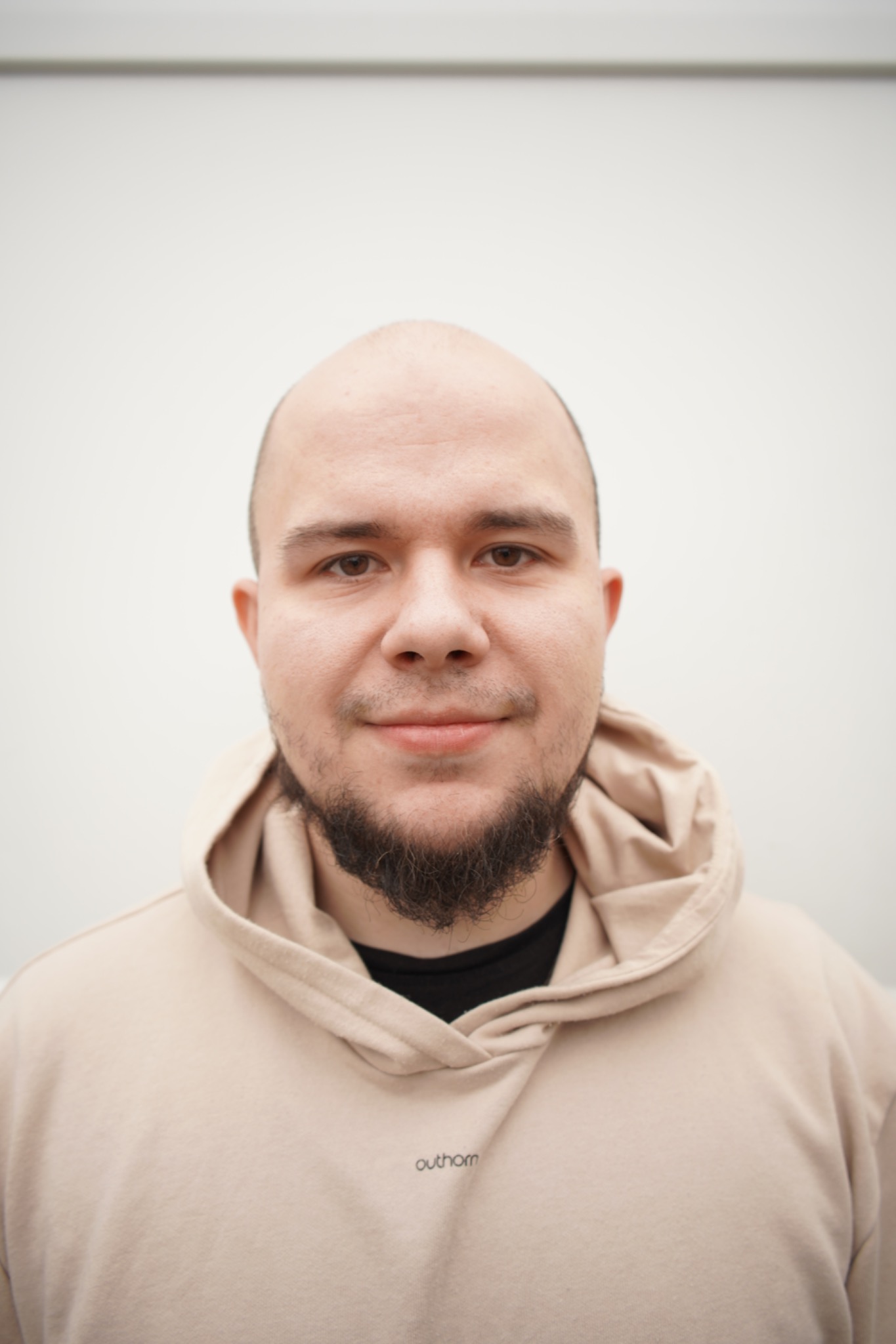 Portret mężczyzny z brodą w beżowej bluzie z kapturem na białym tle.