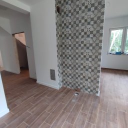 SZTANI Stanisław Mizdal - Ukończone układanie podłogi z płytek imitujących drewno w nowym pomieszczeniu, z fragmentem ściany wykończonej dekoracyjnymi płytkami w stylu patchwork, widoczny otwór w podłodze.
