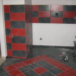 SZTANI Stanisław Mizdal - Układanie płytek podłogowych i ściennych w szachownicę z czerwono-czarnych płytek w trakcie prac wykończeniowych, widoczne narzędzia i wiadro.