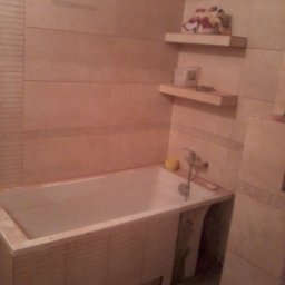 SZTANI Stanisław Mizdal - Wanna obudowana płytkami w trakcie prac wykończeniowych w łazience, widoczne półki z kosmetykami i akcesoriami.