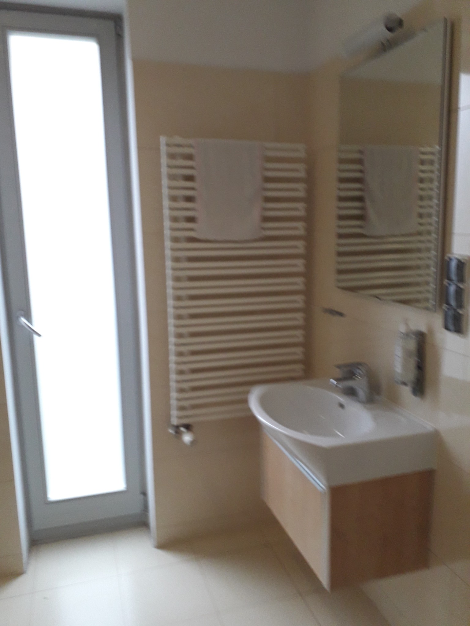 Jasna łazienka z umywalką na szafce, grzejnikiem drabinkowym z ręcznikiem, lustrem i oknem.