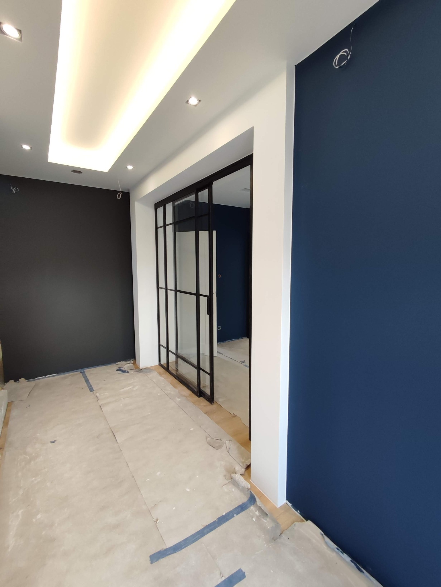 Pokój z pomalowanymi ścianami na granatowo i szaro, z czarnymi przesuwnymi drzwiami szklanymi i zabezpieczoną podłogą przed zabrudzeniem.