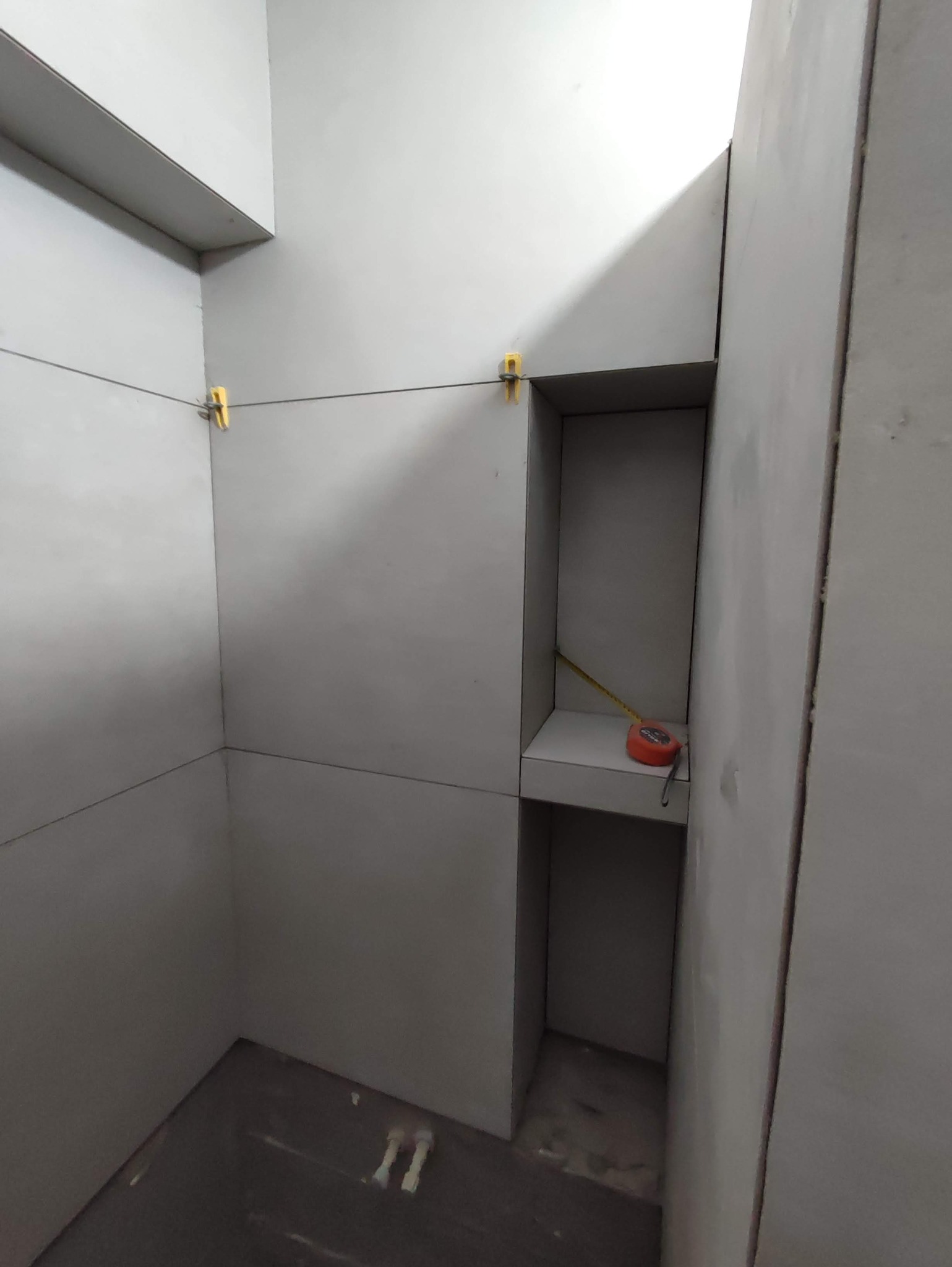 Montaż płyty karton gips w narożniku pomieszczenia, widoczne sznurki z poziomowaniem i miara zwinięta w półce.