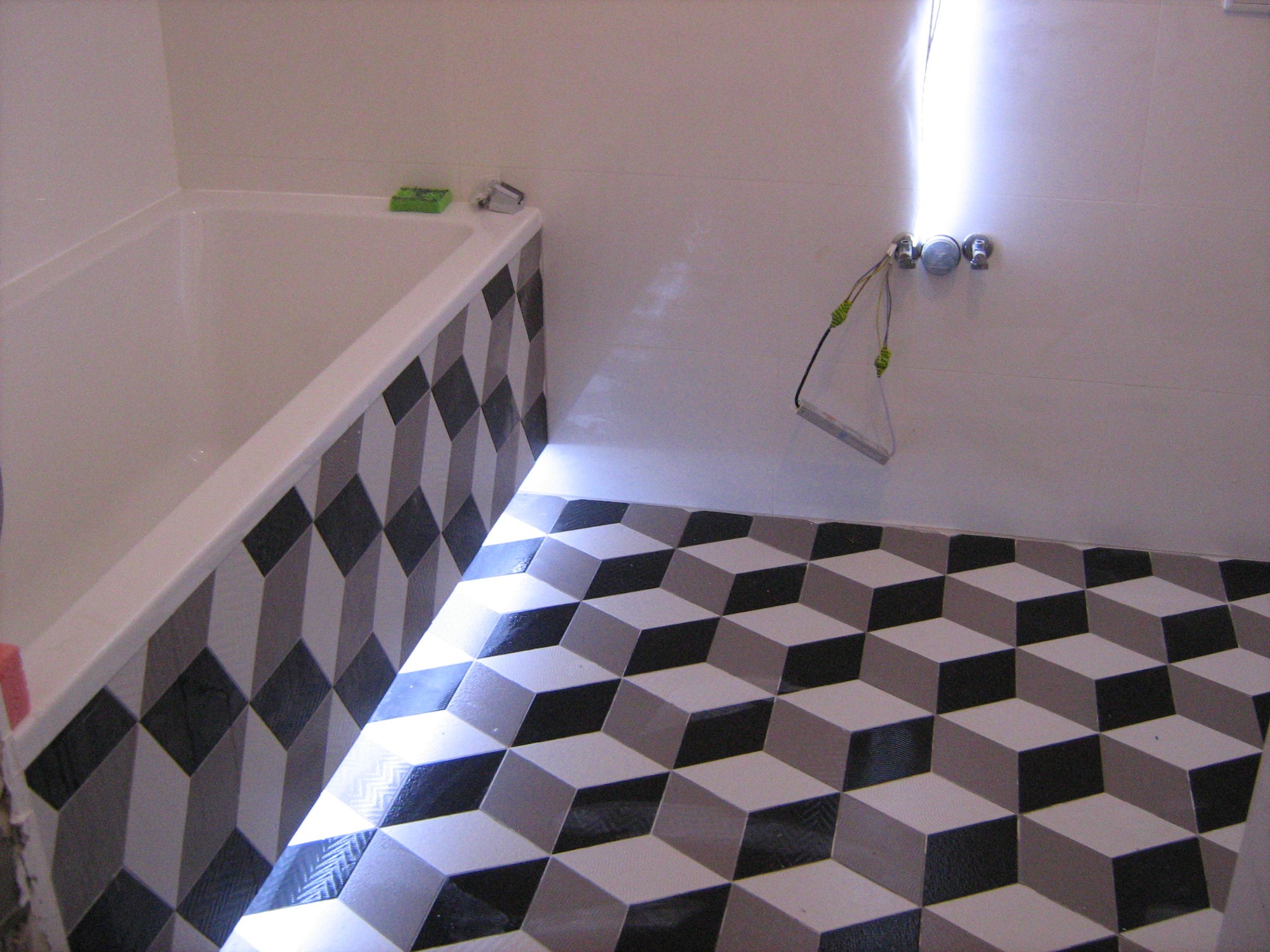 Łazienka z wykończoną podłogą i obudową wanny w geometryczny wzór 3D, widoczne baterie i instalacja oświetleniowa w trakcie montażu.