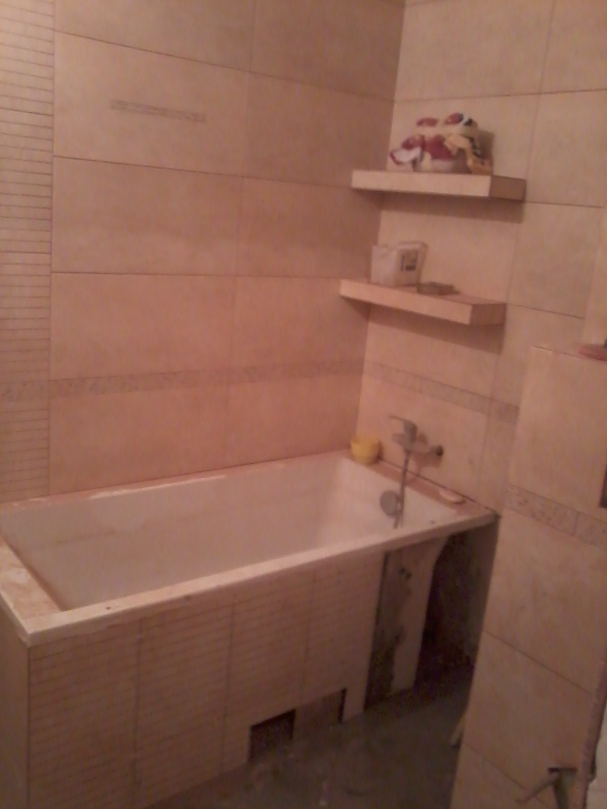 Wanna obudowana płytkami w trakcie prac wykończeniowych w łazience, widoczne półki z kosmetykami i akcesoriami.