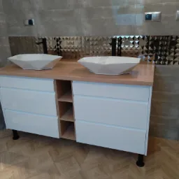 Łazienka z podwójną umywalką w geometrycznych misach na białej szafce z drewnianym blatem, na tle ściany z mozaiką w romby i szarej płytki, podłoga w parkiet ułożony w jodełkę.