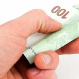 Dłoń trzyma zwinięty banknot 100 euro na białym tle.