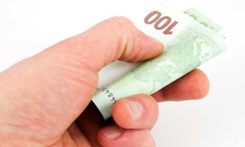 Dłoń trzyma zwinięty banknot 100 euro na białym tle.