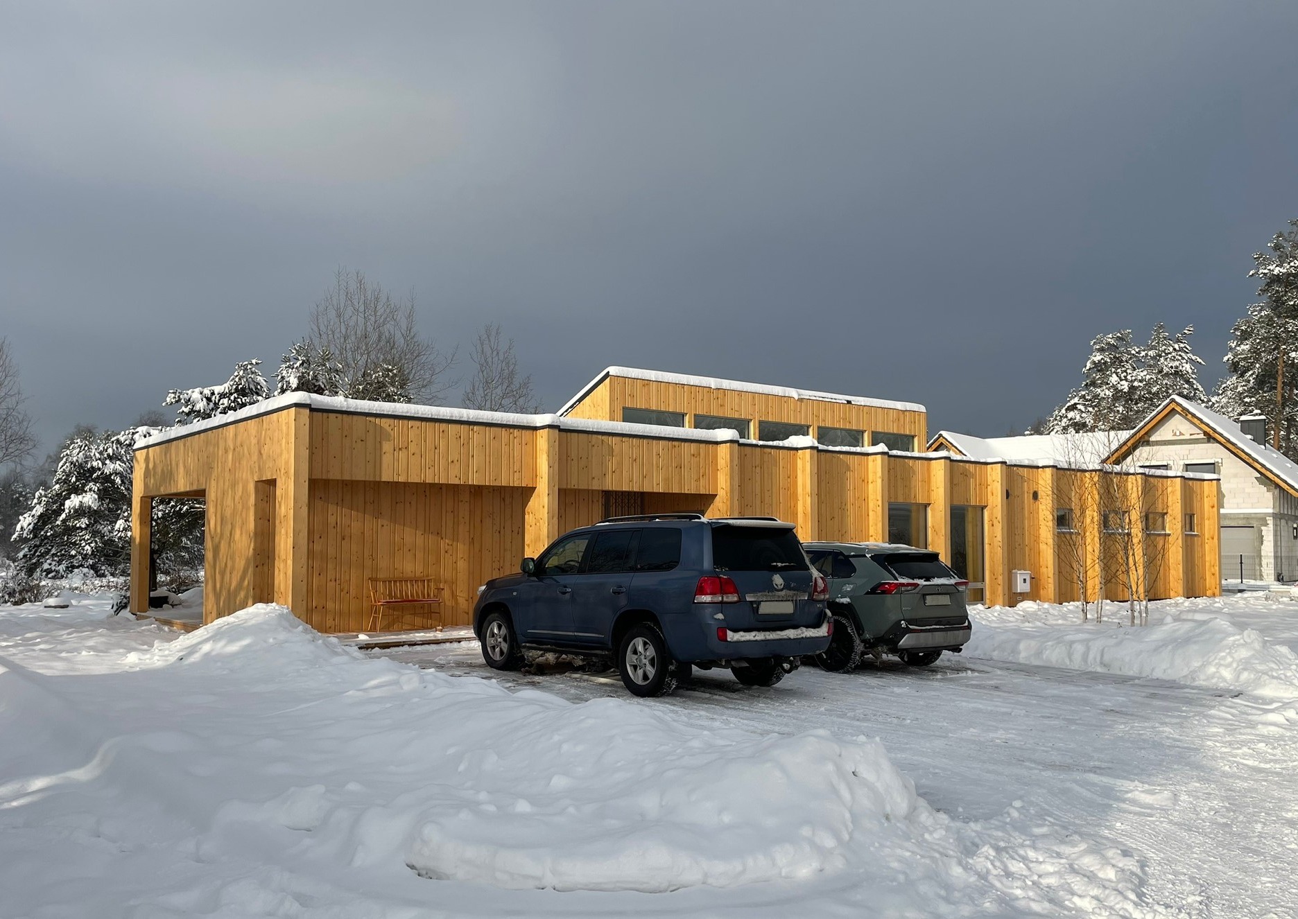 Nowoczesny dom jednorodzinny z drewnianą elewacją w zimowej scenerii, z zaparkowanymi dwoma samochodami.