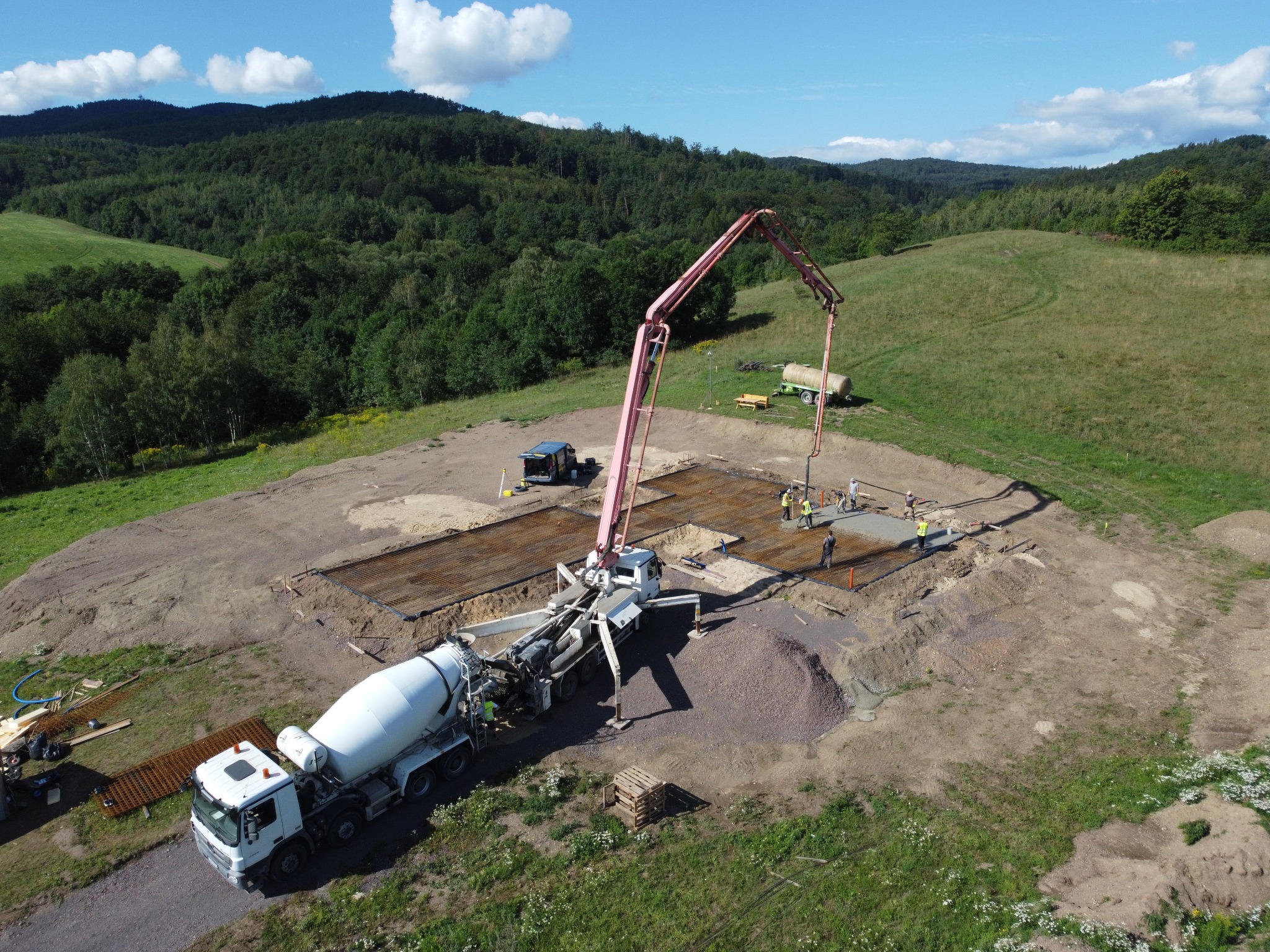 Betonowanie płyty fundamentowej z użyciem pompy do betonu, widok z drona na plac budowy otoczony zielenią.