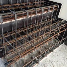 Zbrojenie schodów z prętów stalowych, częściowo skorodowanych, w drewnianym szalunku, przygotowane do zalania betonem.
