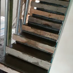 Surowe drewniane szalunki schodów wypełnione świeżym betonem w trakcie budowy, widoczne metalowe rury i elementy konstrukcyjne w tle.