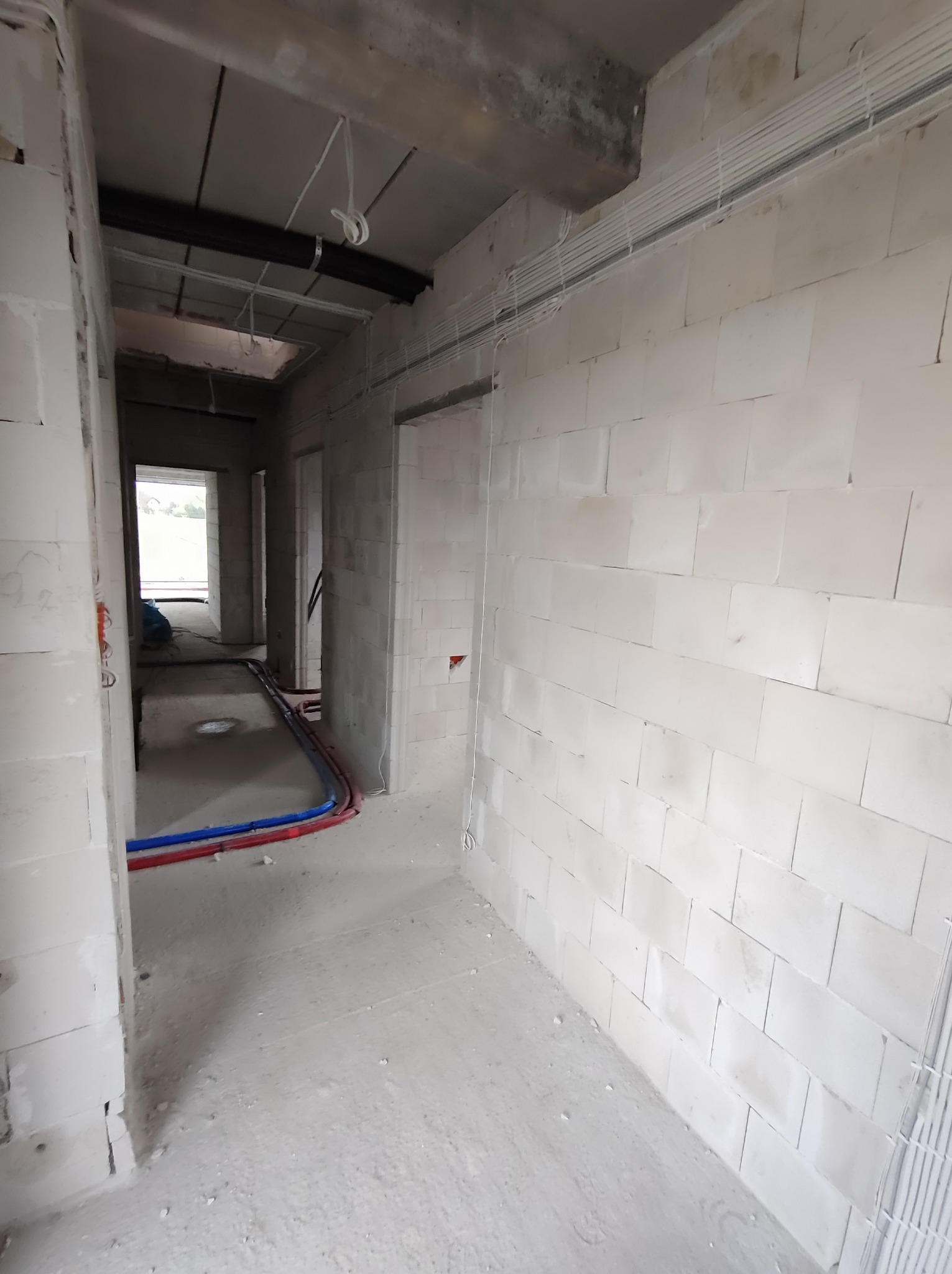 Wnętrze surowego domu w trakcie budowy, widoczne kable i rury instalacyjne, ściany z białego betonu komórkowego, brak wykończenia.