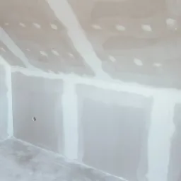 Wnętrze poddasza z zamontowanymi płytami gipsowo-kartonowymi, widoczne szpachlowane łączenia, przygotowane do dalszych prac wykończeniowych.